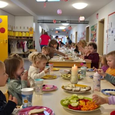 Kinder sitzen an einem gedeckten Tisch und freuen sich über das Essen