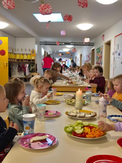 Kinder sitzen an einem gedeckten Tisch und freuen sich über das Essen