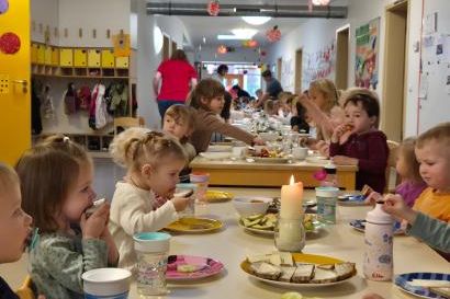 Kinder sitzen an einem gedeckten Tisch und freuen sich über das Essen